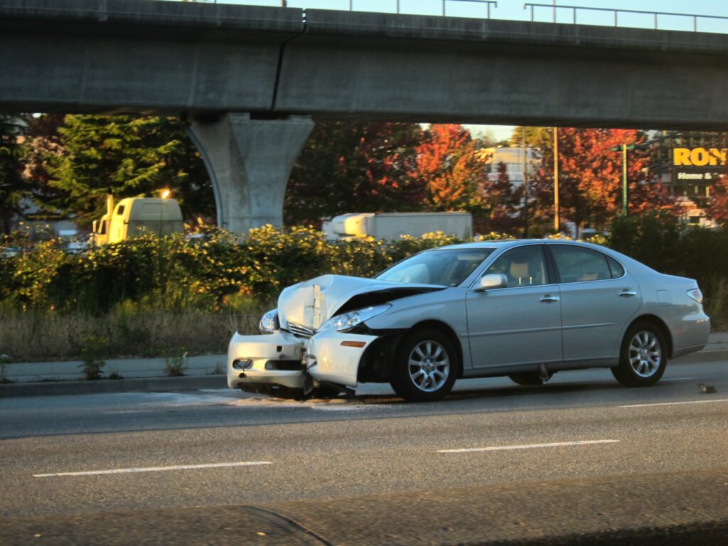 A car with its front end crumpled on a road beside an elevated highway