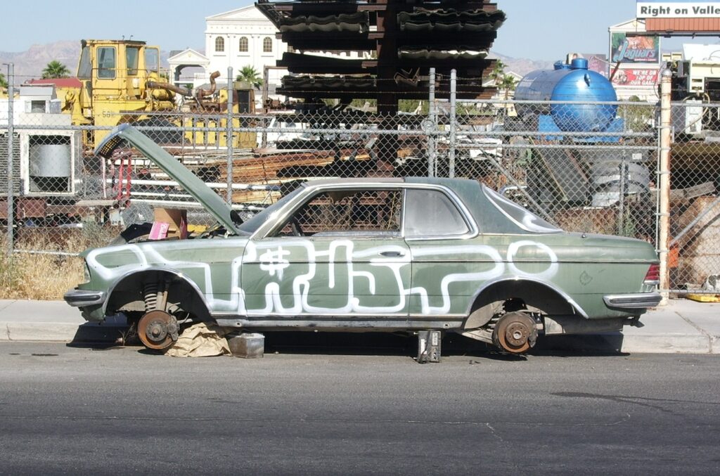 A car with no tires and rusty wheels, hood open, and the word trust written across the driver side