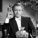 The actor Claude Rains in dinner attire smoking a cigarette, playing a character in the film Deception.